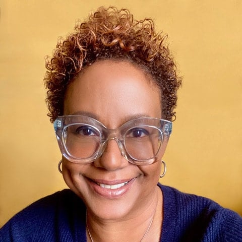 A portrait of Harriette Cole, a dark skinned woman with short blonde curly hair and translucent blue glasses.